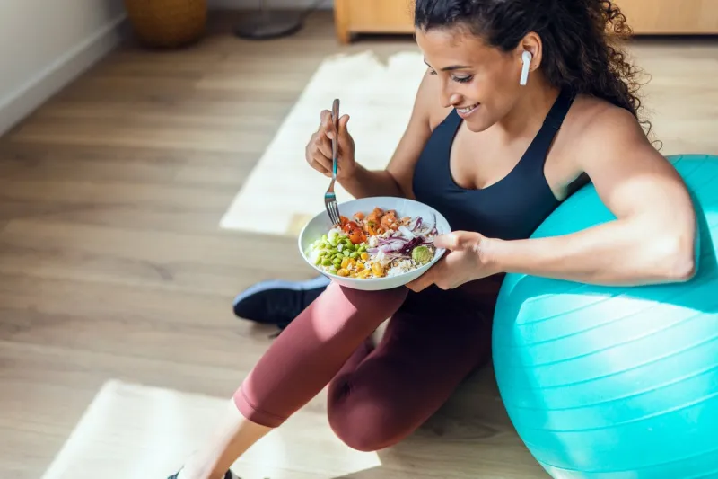 shot of sporty young woman eating healthy while listening to music sitting on the floor at home