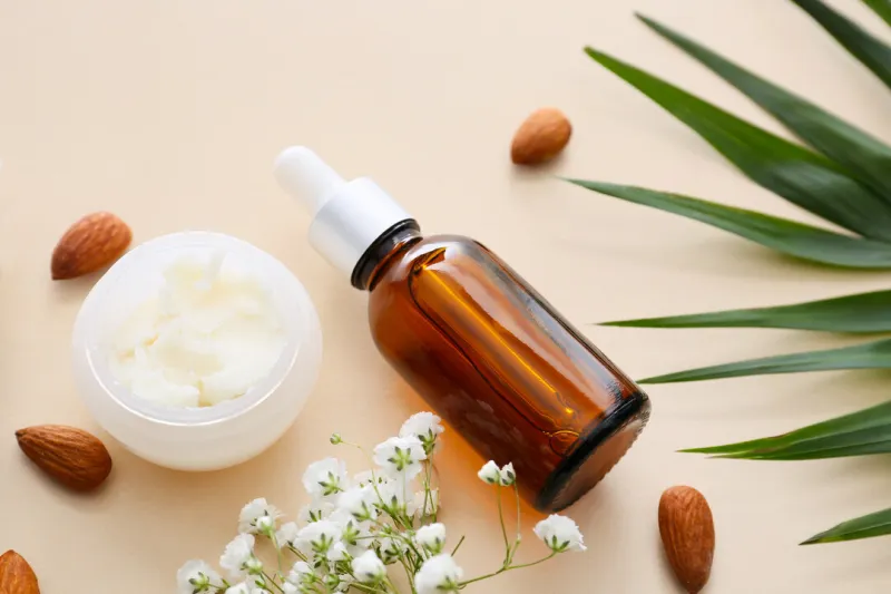 bottle of almond essential oil and cream on light background