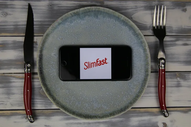 viersen, germany - may 9 2020  closeup of mobile phone on plate and wood table, cutlery with logo lettering of slimfast food company (focus on center)