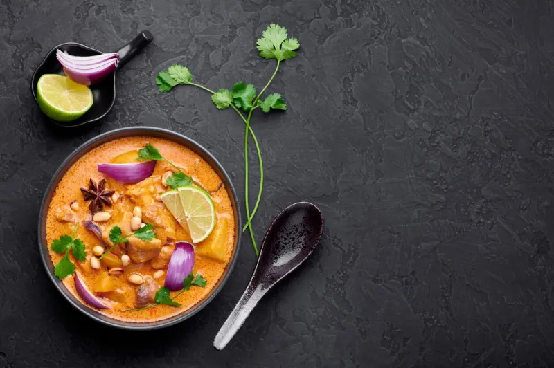 a chicken massaman curry in black bowl at dark slate background massaman curry is thai cuisine dish with chicken meat, potato, onion and many spices thai food copy space top view
