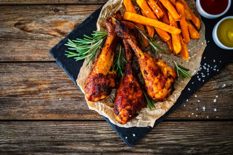 roasted chicken drumsticks with sweet potatoes french fries and ketchup, mayonnaise, mustard on wooden table