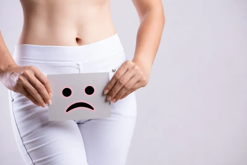 closeup young woman holding paper with sad smiley face or unhappy near her crotch lower abdomen medical or gynecological problems, healthcare concept
