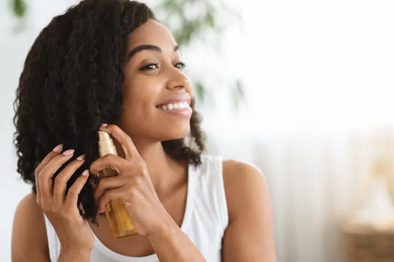 hair care happy afro woman using oil for split ends while getting ready at home, closeup image with copy space