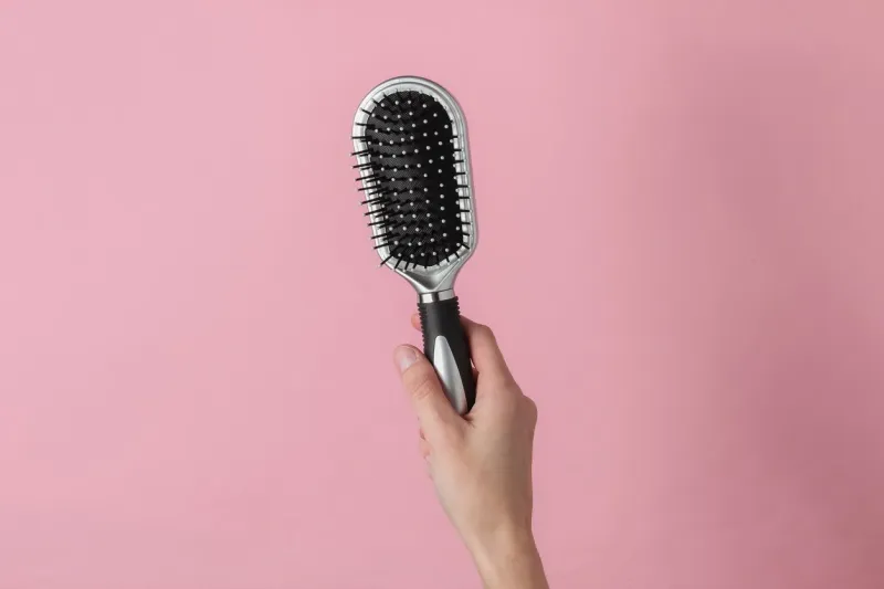 female hand holds a comb on a pink pastel background hair care beauty concept