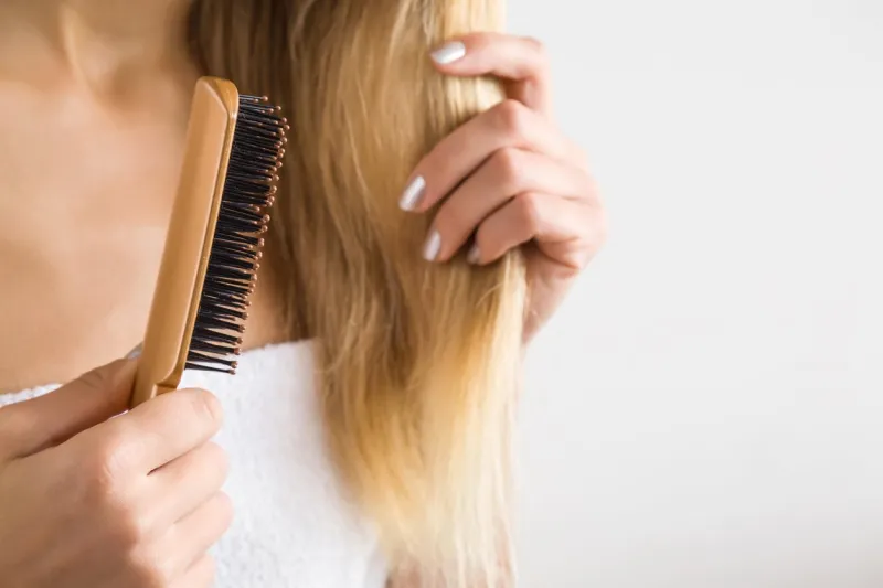 woman's hand brushing blonde hair cares about a healthy and clean hair beauty salon empty place for a text on the gray background