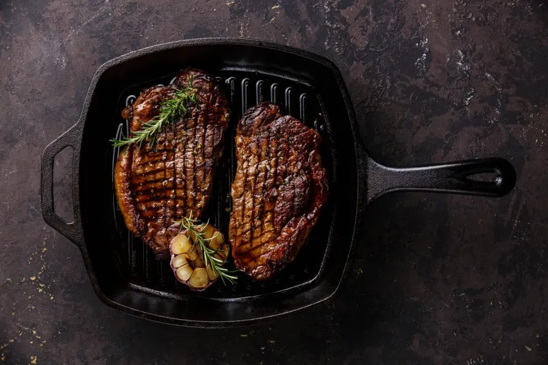 grilled black angus steak striploin on frying cast iron grill pan on dark background