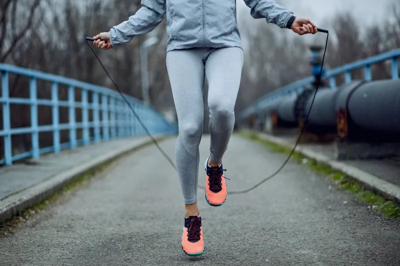 unrecognizable female athlete exercising with jump rope while having a sports training outdoors