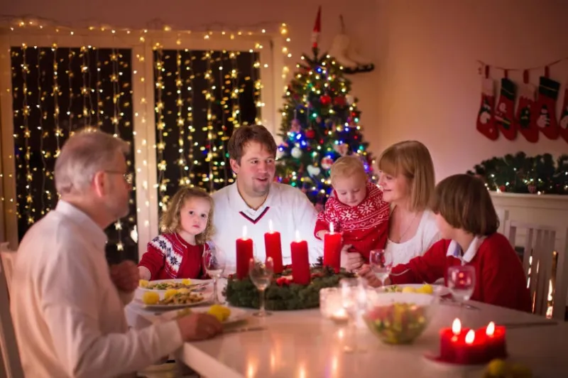 grande famille avec trois enfants célébrant noël à la maison dîner festif à la cheminée et l'arbre de noël parents et enfants mangeant à la cheminée dans la salle décorée éclairage de l'enfant bougie de l'avent bougie