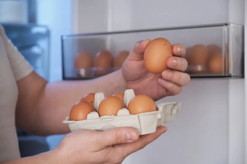 close up of a man placing eggs in the fridge door shelf
