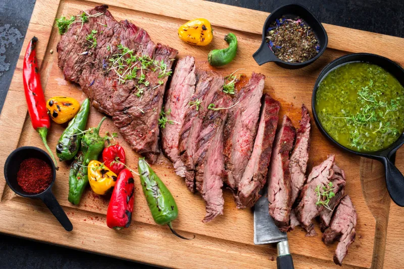 modern design barbecue dry aged wagyu bavette de flanchet steak with chili and chimichurri sauce as top view on a wooden cutting board