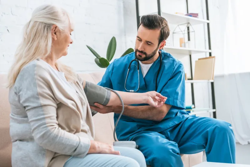 young male nurse measuring blood pressure to senior woman