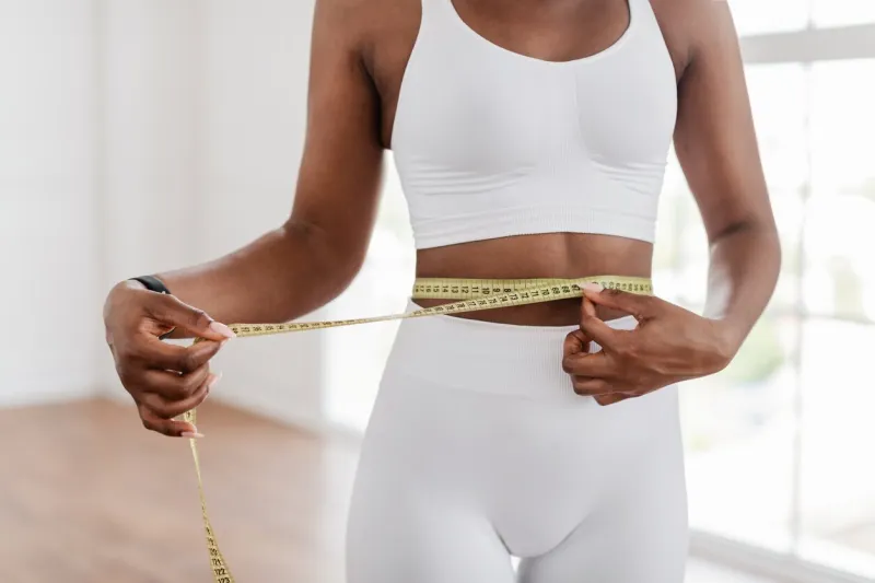 weight loss concept closeup cropped view of unrecognozable fit african american lady measuring her waist using yellow tape, blurred background slim black woman checking her body parameters