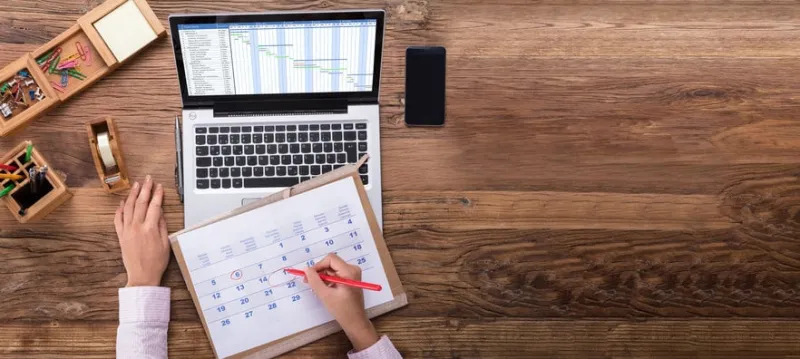 an overhead view of businesswoman marking date on calendar with gantt chart on laptop screen