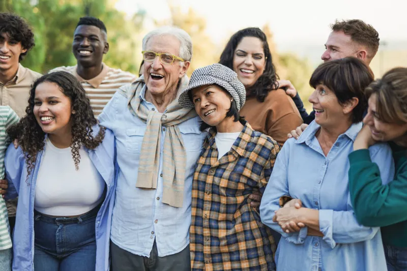 group of multigenerational people having fun hugging each other outdoor - crowd of multiracial friends enjoy day at city park