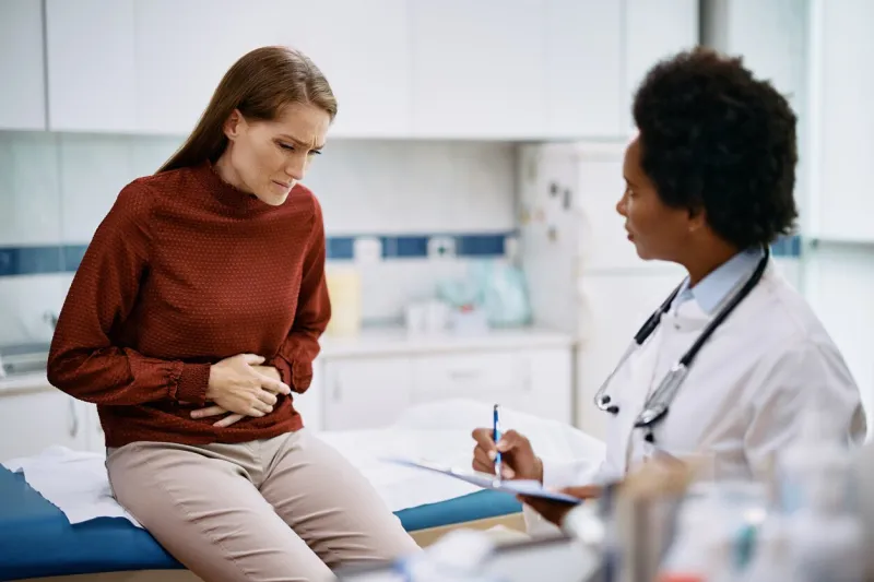 female patient holding her abdomen in pain while talking to her doctor at medica clinic