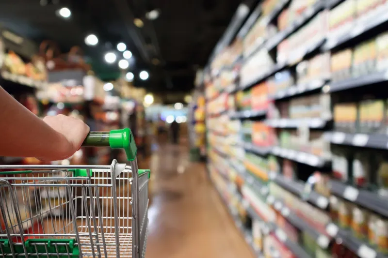 woman hand hold shopping cart with abstract blur supermarket aisle background