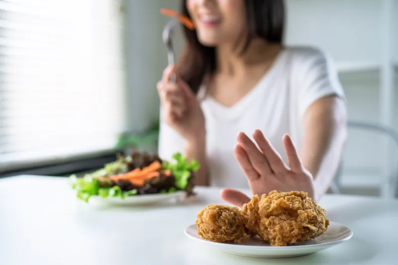woman on dieting for good health concept, young women use hands to push fried chicken and choose to eat vegetables for good health