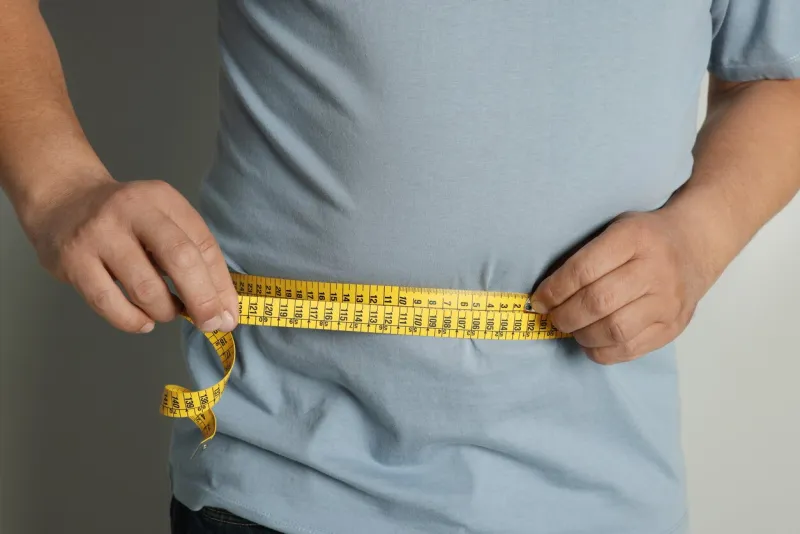 man measuring waist with tape on grey background, closeup