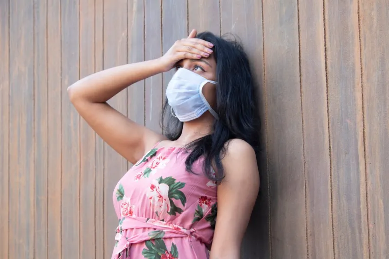 worried coronavirus infected woman wearing protective mask and checking her temperature by touching her forehead with palm of hand