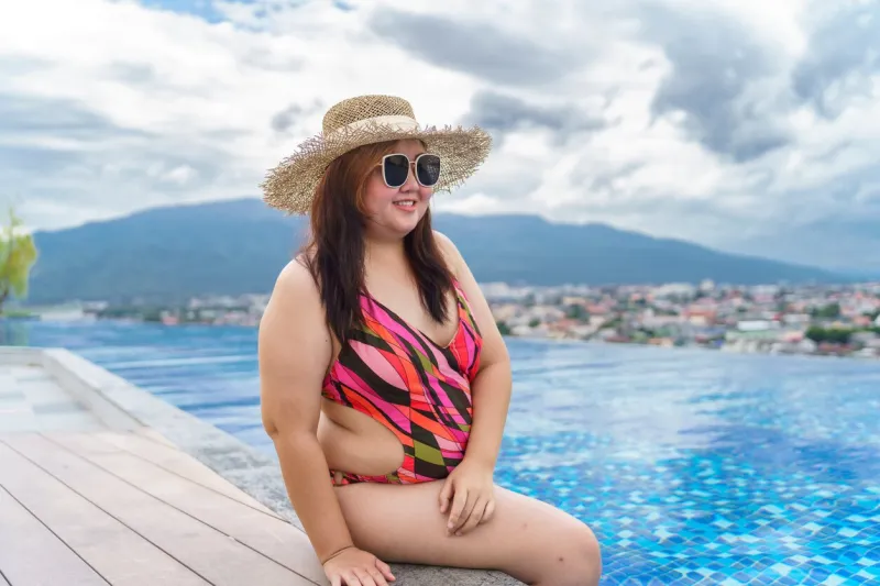 overweight young asian woman wearing orange swimsuitÂ and straw beach sun hat relaxing in pool happy plus size woman cheery funny vacation traveling in summer