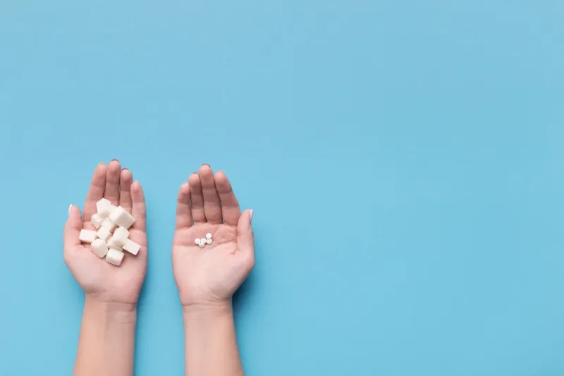 female hands with sugar and pills on blue background choice of sweetener in tablets or regular sugar alternative to sugar for diabetics