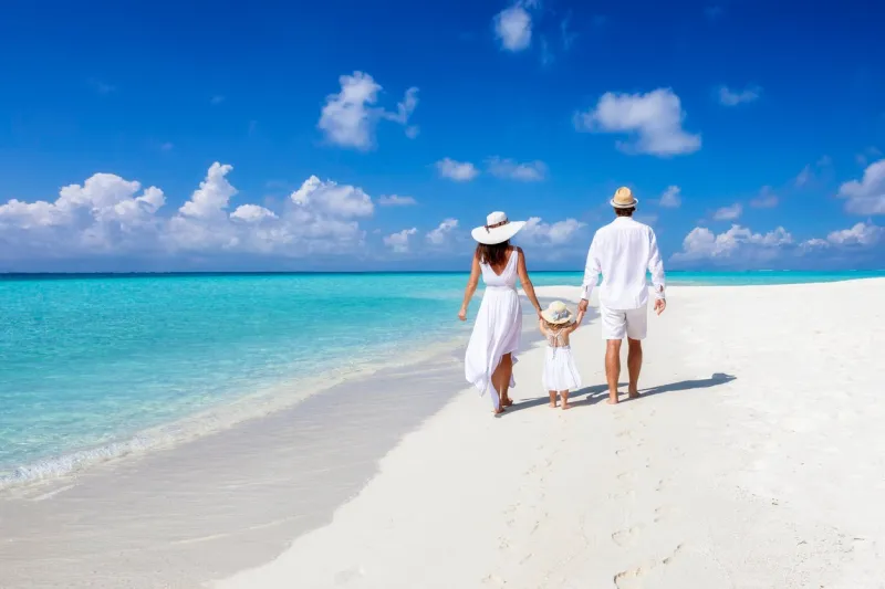 a beautiful family walks together on a tropical paradise beach in the maldives with turquoise ocean and white sand during their vacation time