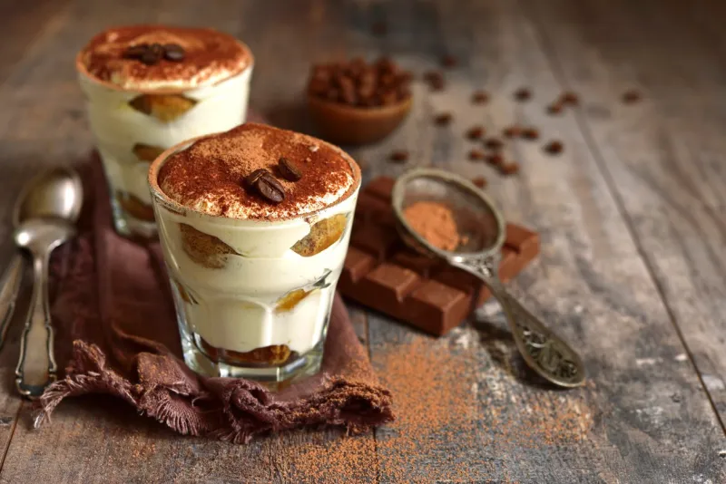 homemade traditional italian dessert tiramisu with mascarpone cheese,savoyardi biscuit,coffee and whipped cream in a glasses over dark wooden background