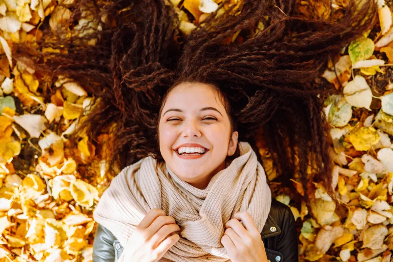 portrait of beautiful smiling ypung woman lying over yellow leaves at autumn park