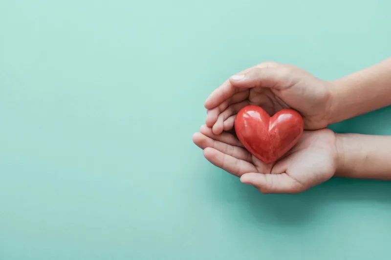 hands holding red heart on blue background, health care, love, organ donation, family insurance and csr concept, world heart day, world health day