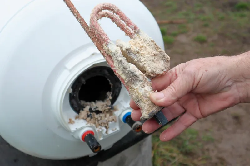 repair and maintenance of boilers the plumber pulls the tubular electric heater out of the hole in the boiler lime deposits on stainless steel heating element and anode