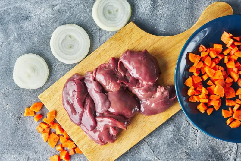 raw fresh liver on a plate with chopped vegetables onions and carrots gray background