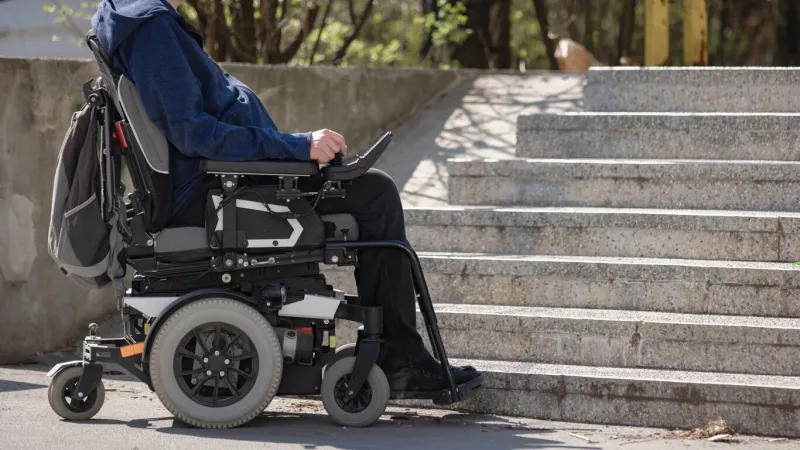 person with disability on electric wheelchair stopping at the bottom of inaccessible staircase, unable to reach the top