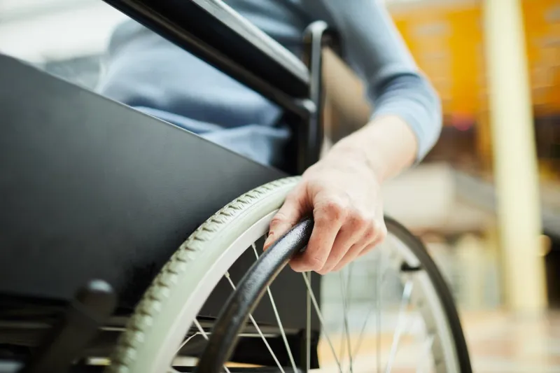 close-up of young female patient sitting in wheelchair and holding the wheel while going at hospital