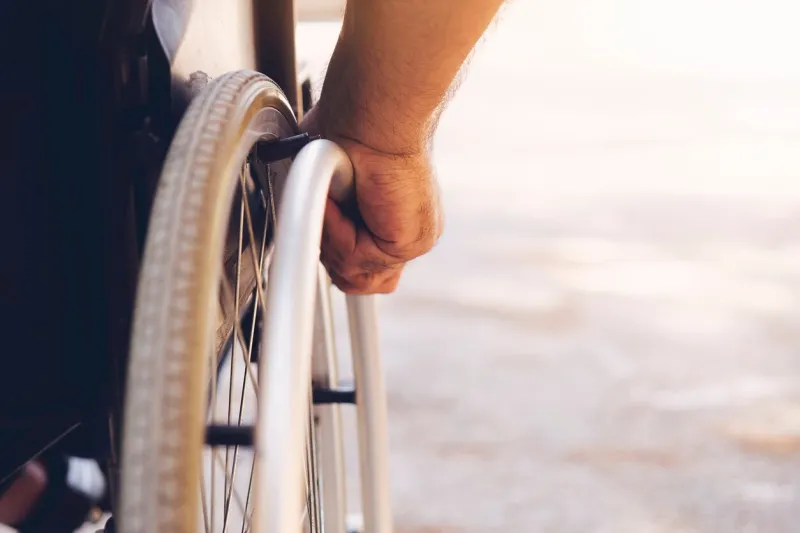 closeup photo of young disabled man holding wheelchair outside in nature