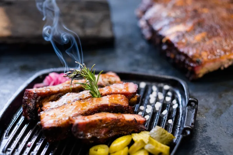 grill restaurant menu closeup of smoked pork ribs, served in griddle pan and decorated with burning rosemary twig