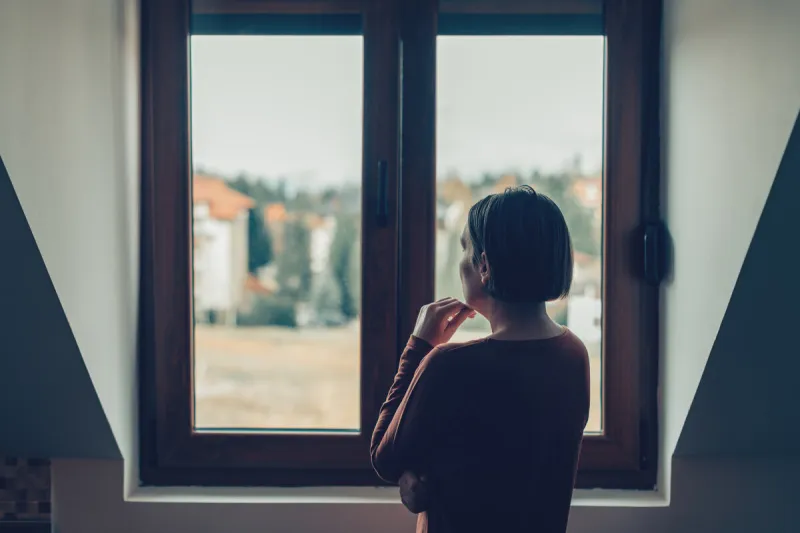 sad woman looking out of the window in loft apartment
