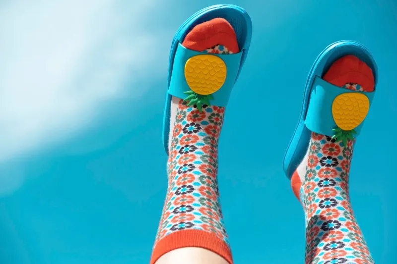 a young woman in colorful patterned socks and blue flip-flops face down against the sky summer concept