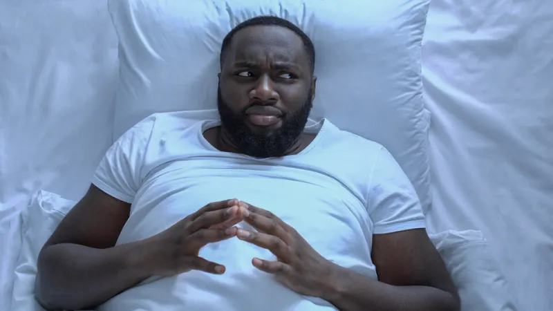 nervous man drumming fingers lying in bed, erectile dysfunction