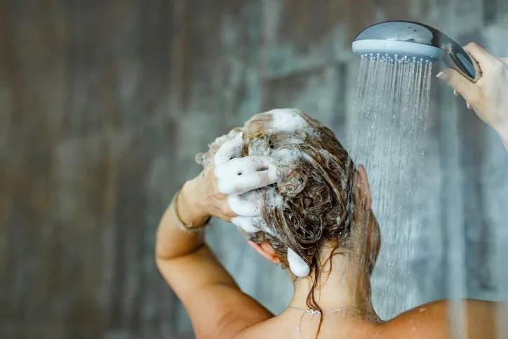back view of a woman washing her hair with a shampoo in bathroom copy space