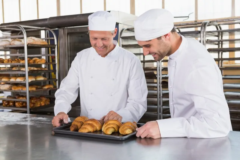 smiling bakers looking trays of croissants