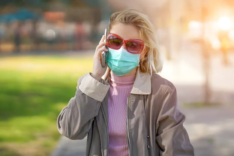 portrait of woman wearing medical mask in street in city and speaks on the phone woman walking on the street wearing protective mask as protection against infectious diseases