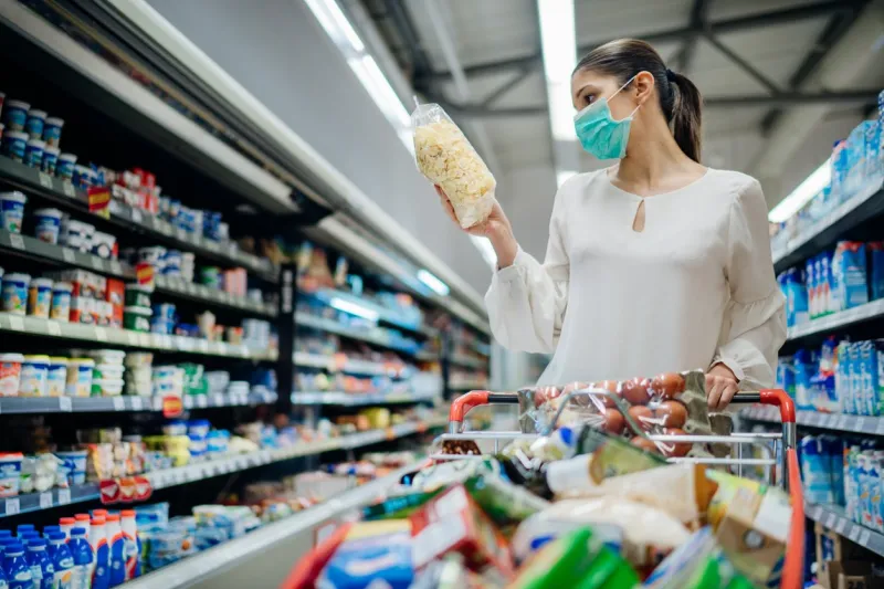 young person with protective face mask buying groceries supplies in the supermarketpreparation for a pandemic quarantine due to coronavirus covid-19 outbreakchoosing nonperishable food essentials