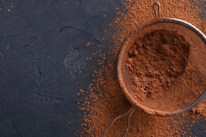 culinary sweet background closeup of sifted cocoa powder in a sieve on black slate ingredients for making brownies mockup for pastry classes top view, copy space