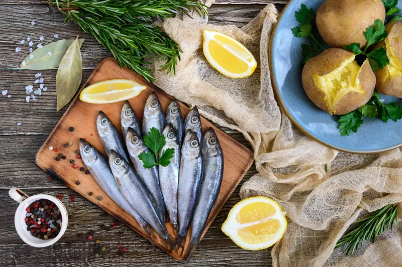 boiled unpeeled potatoes in skins, a small salted fish of baltic herring, sprats on a wooden table top view flat lay