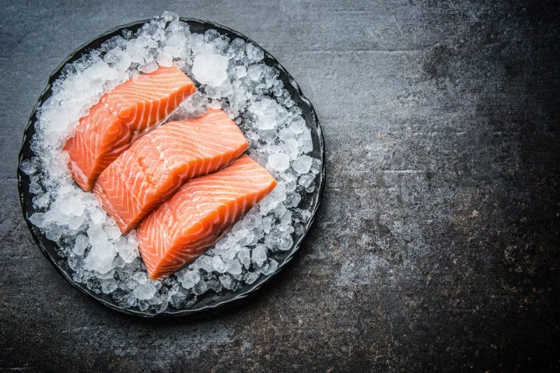 portioned raw salmon fillets in ice on plate - top of view