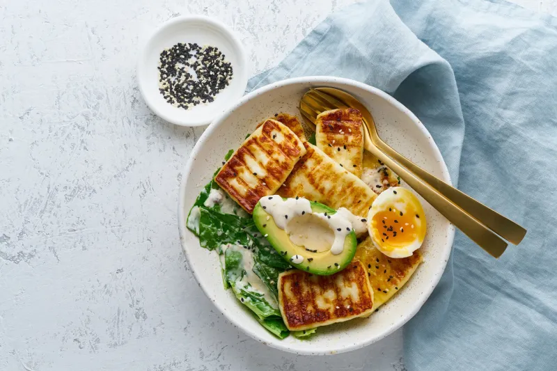 keto ketogenic diet soft boiled eggs with grilled haloumi, avocado and lettuce, mediterranean cuisine on pastel background