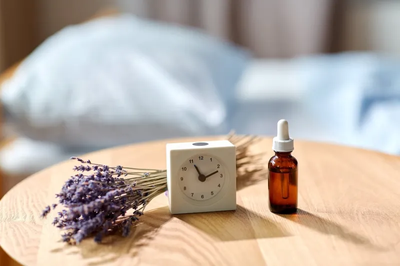 sleep disorder, bedtime, sleeping and morning concept - close up of alarm clock and lavender essential oil on night table at home