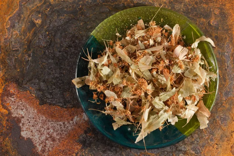 dried lime blossoms on a blue-green glass plate rusted steel in the background, top view