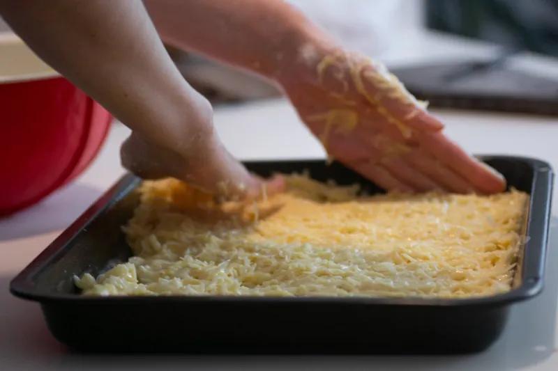female hands spread a mixture of grated potatoes and flour in a pan
