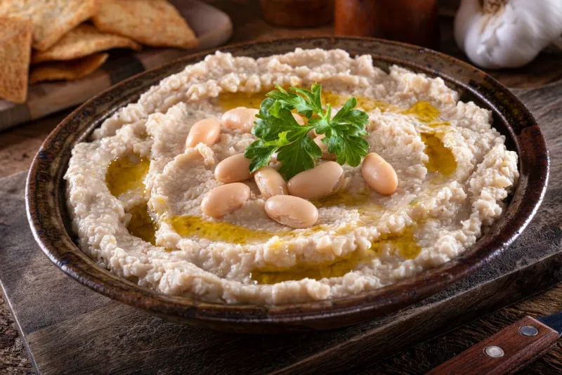a bowl of delicious tuscan style white bean and garlic dip on a rustic table top
